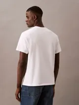 Remera blanca de algodón con cuello redondo y manga corta. Estampado frontal con el logo de Calvin Klein en rojo.