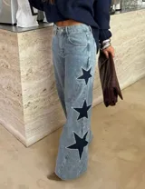 Jean de tiro alto con pierna amplia de corte recto, confeccionado en denim de lavado claro. Presenta aplicaciones de estrellas en contraste con bordes decorados con tachas metálicas.