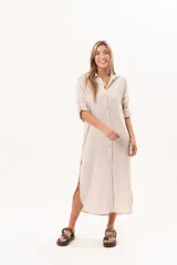 Vestido camisero largo de lino color beige, con silueta relajada, abotonado al frente, cuello camisero, mangas regulables y tajos laterales.
