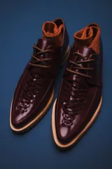 Zapato acordonado de cuero color burdeos, con detalle de trenzado en la parte delantera y suela de goma color crema.