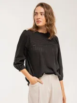 Blusa negra de algodón con escote redondo, manga tres cuartos y silueta oversized. Presenta bordados y texturas combinadas.