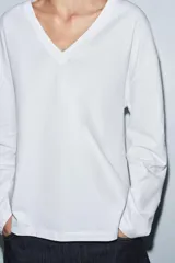 Camiseta blanca de algodón con escote en pico, manga larga y bajo recto.