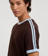Remera de algodón color celeste con cuello redondo y bordes de mangas en color blanco. Presenta diseño de rayas dobles blancas en los hombros y mangas.