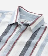 Camisa de hombre de manga corta con cuello tradicional y abotonado frontal. Presenta un tejido texturizado con un patrón de rayas verticales en tonos beige, blanco y marrón claro.