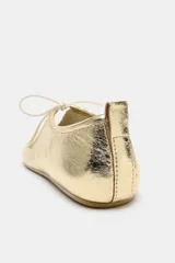 Zapato tipo bailarina de piel con acabado metalizado dorado, detalle de lazo frontal y tirador en el talón.