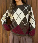 Sweater de lana merino con diseño clásico de rombos en tonos chocolate, crudo y bordeaux. Presenta cuello redondo, mangas largas y puños y ruedo acanalados.