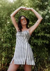 Minivestido de algodón y lino a rayas verticales blancas y grises con mini bordados. Tiene elástico en la espalda, tirantes finos y tajos en el frente.