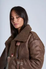 Campera gamulán marrón de símil cuero, con interior de corderoy al tono, cierre frontal con cremallera y cuello con solapas grandes. Presenta detalles de hebillas en los puños y bolsillos laterales con cierre.