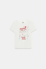 Camiseta blanca de algodón con cuello redondo, manga corta y calce regular. Presenta un estampado frontal ilustrado con conejos, corazones, estrellas y el texto "Kindness for every kind".