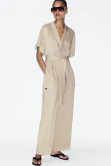 Mono largo de cuello solapa y escote en pico cruzado, con mangas cortas. Presenta bolsillos laterales de plastrón con solapa y botones, y un cinturón del mismo tejido para ajustar en la cintura. Cierre frontal con cremallera y botón interior.