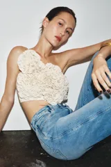 Top crop color blanco hueso con escote recto y hombros descubiertos. Presenta una aplicación de flores tridimensionales en relieve cubriendo toda la parte delantera.