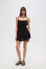 Vestido corto de algodón color blanco, con breteles finos tipo lencero, escote recto con detalle de volado y cintura con elástico fruncido. La falda presenta un diseño holgado con volado en el ruedo.