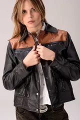 Campera de cuero negra de corte recto, con detalles en cuero marrón tostado en los hombros y canesú. Cuenta con múltiples bolsillos frontales con solapa, cierre de botones a presión y tachas metálicas decorativas.
