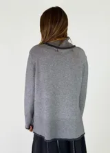Sweater de cuello alto en color beige, con diseño de punto liso y terminaciones acanaladas en puños y ruedo. Presenta aberturas laterales en el bajo y un detalle de borde desflecado en el ruedo y los puños.