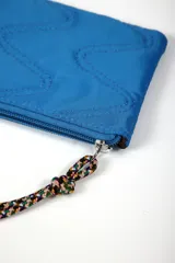 Billetera rectangular de color azul, con diseño acolchado de costuras en zigzag y cierre superior con tirador de cordón trenzado multicolor con punteras naranjas.