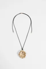 Collar largo con cordón negro y dije colgante metálico dorado con forma de flor o concha marina texturizada.