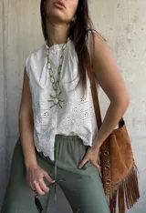 Camisa sin mangas blanca de broderie, con cuello alto fruncido y cierre frontal con botones.