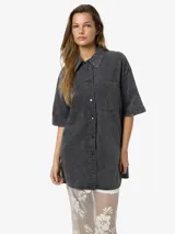 Vestido camisero corto de denim negro con lavado ácido, manga corta, cierre frontal con botones, dos bolsillos con solapa en el pecho y corte holgado.