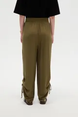 Pantalón verde militar de corte ancho y tiro alto, con cintura elástica fruncida y detalles de cordones ajustables en los tobillos.