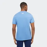 Remera deportiva de manga corta, color azul claro, con cuello redondo y un bolsillo abierto en el pecho. Presenta una costura horizontal que cruza el pecho y el logo de la marca en el frente.