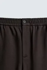 Pantalón regular fit color marrón oscuro, confeccionado en tejido con viscosa. Cuenta con cintura elástica, bolsillos delanteros y detalle de bolsillos traseros de vivo. El cierre frontal es con cremallera y botón.