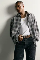 Camisa de algodón con corte boxy fit, diseño a cuadros en tonos grises y blancos, cuello clásico y manga larga con puños abotonados.
