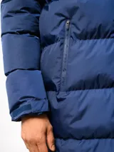 Parka larga acolchada color azul marino con capucha, cierre frontal con botones a presión y bolsillos laterales. Presenta el logo de Umbro y el escudo del Club Nacional de Football bordados en el pecho.