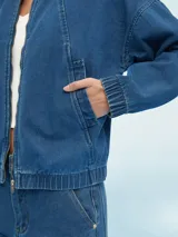 Campera bomber de denim azul con cierre frontal, bolsillos laterales y elástico en puños y cintura.