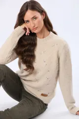 Buzo tejido de punto en color beige, con cuello redondo, mangas largas y puños acanalados. Presenta un delicado diseño bordado con motivos florales dispersos en el frente y una etiqueta de cuero sintético en el ruedo.