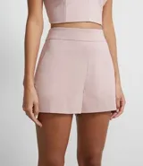 Short corto de vestir color rosa pálido, de tiro alto y corte recto. Presenta un diseño de falso cruce frontal que simula un short cruzado o falda pantalón.