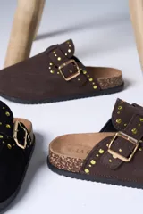 Zueco de gamuza color marrón chocolate, con detalle de tachas doradas y hebilla metálica ajustable en el empeine. Presenta una base de corcho y suela de goma antideslizante.