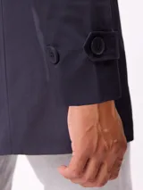 Gabardina de corte clásico en color beige, con cierre frontal de cremallera y botones, cuello camisero y puños ajustables con trabillas.
