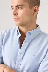 Camisa celeste de manga larga con cuello abotonado y cierre frontal de botones. Confeccionada en algodón con sutil bordado en el pecho.