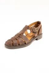Sandalias tipo cangrejera de cuero color marrón, con diseño de tiras cruzadas, talón cerrado y tira ajustable con hebilla metálica y detalle de estrella grabada en el lateral. Suela plana con pequeño tacón.