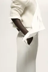 Pantalón de vestir blanco con cintura clásica, cierre con botón oculto y corchete. Presenta bolsillos al bies, bolsillo trasero decorativo y piernas amplias con pliegues marcados adelante y atrás.