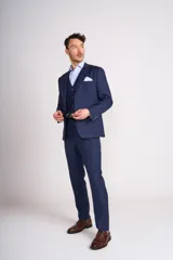 Traje de tres piezas color azul marino con textura sutil. Incluye saco entallado con solapas clásicas, chaleco abotonado y pantalón de corte recto. Se complementa con una camisa celeste de cuello italiano y pañuelo de bolsillo blanco.