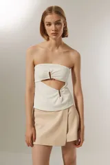 Top strapless color blanco, con diseño cut-out frontal y detalle de aros metálicos en el centro. Presenta un ajuste al cuerpo y cierre posterior.