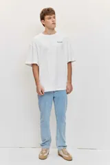 Remera oversize blanca de manga corta, con cuello redondo y pequeño texto estampado en azul en el pecho.