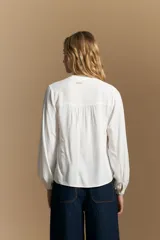 Camisa de manga larga color blanco, con cuello mao y escote en V. Presenta frunces en el canesú, cierre frontal con botones y mangas amplias con puños abotonados.