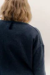 Buzo de lambswool color beige, con escote redondo y detalle en V. Presenta cierres metálicos en los puños que revelan un interior en contraste de color marrón y ribete rojo. Tiene tajos laterales para mayor comodidad y un fit amplio.