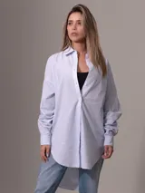 Camisa de algodón de corte oversized, color celeste con finas rayas verticales blancas. Presenta cuello clásico, cierre frontal de botones y dobladillo curvo.