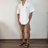 Camisa de manga corta con cuello cubano, confeccionada en tejido texturizado de color negro. Presenta cierre frontal con botones y un pequeño logo bordado en el pecho.