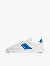 Zapatillas deportivas de estilo vintage Tommy Jeans modelo The Greenwich, confeccionadas en ante color blanco con paneles laterales en azul vibrante y detalles en gamuza gris claro. Presentan cierre con cordones, suela cupsole de goma y logo de la marca en el lateral.