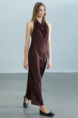 Vestido midi de tejido satinado en color marrón oscuro, con cuello halter de escote fluido, hombros descubiertos y cierre posterior con botones.