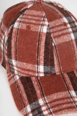 Gorro tipo baseball de tela escocesa afelpada en tonos marrón, blanco y gris.