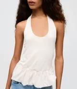 Blusa de algodón color blanco con diseño frente única, bretel posterior y ruedo con volado peplum que aporta volumen. Presenta un corte ajustado en el torso y silueta moderna.