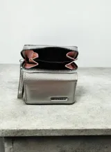 Billetera compacta de diseño plegable en color celeste, con textura granulada. Presenta una placa metálica dorada con el logo de la marca en el frente y una pequeña correa lateral del mismo tono.