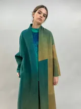 Tapado largo de lana merino afieltrada con diseño de paneles en degradé de tonos verdes y ocres. Presenta hombros caídos, mangas rectas, bolsillos laterales y cierre frontal con broches ocultos.