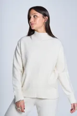 Sweater color beige de tejido de punto con cuello alto y mangas largas. Presenta detalles de ochos en diagonal en los laterales.