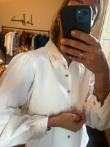 Camisa de denim blanco con mangas abullonadas, cuello clásico con detalle bordado y cierre frontal con botones.